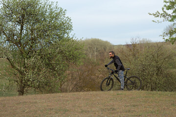 Sports brutal bearded guy on a modern mountain bike. Cyclist on the green hills in the spring.