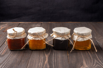jars of jam and honey with paper caps in a row on a dark wooden background