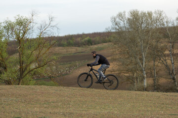 Obraz premium Sports brutal bearded guy on a modern mountain bike. Cyclist on the green hills in the spring.