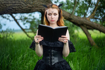 Fototapeta premium Young beautiful witch in black dress conducts a ceremony in a green forest on a summer day. Modern witchcraft.