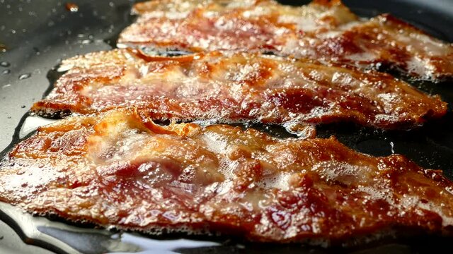 Fry the bacon in a pan. A slice of pork bacon is prepared in its own fat. Layer of meat and lard. Close up in the kitchen.