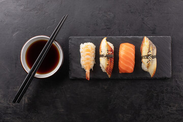 Sushi set on a slate board, soy sauce in a bowl and chopsticks on the side. Japanese traditional food on black background, top view