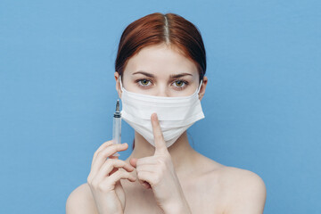 emotional woman with syringe in hand and medical mask injection vaccine blue background
