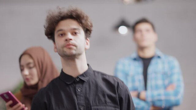 Young millennial Middle Eastern man waiting in queue talking and messaging online on smartphone. Caucasian and Muslim people waiting in line indoors. Urban lifestyle.