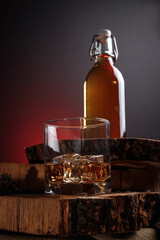 A glass of alcohol near a bottle. Old whiskey bottle on black wooden table. Drinks on a dark blurred background.