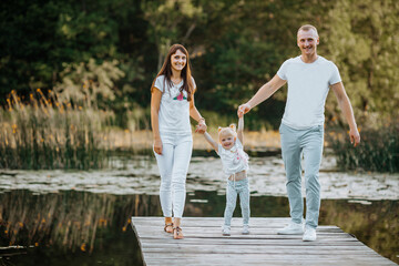 Friendly happy family walking along the wooden pier on the lake holding hands.