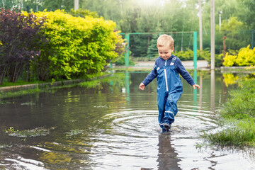 Little cute playful caucasian blond toddler boy enjoy have fun playing jumping in dirty puddle...