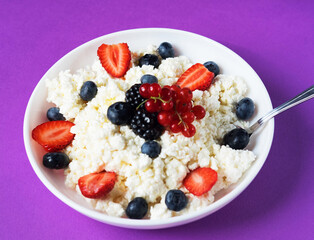 Cottage cheese with fresh strawberries and blueberries in a bowl for healthy breakfast over purple background. top view.