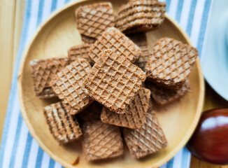 Many square chocolate brown waffles lie on a wooden plate in centre. Wooden spoon. Place for text.
