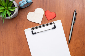 blank clipboard over wooden desk, decorated heart symbol. above view. valentine goals card template. love contract conceptual