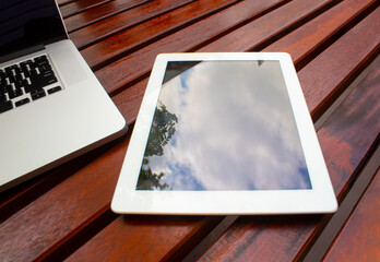 A Tablet on a wooden table next to a laptop.