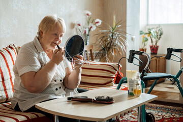 Senior beauty and skincare. Senior elderly plus size blonde woman with Disability applying lipstick near mirror at home.