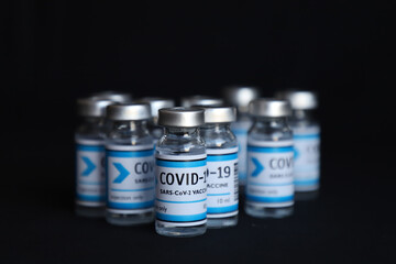 COVID 19 vaccine injection bottles on black background - mid range shot