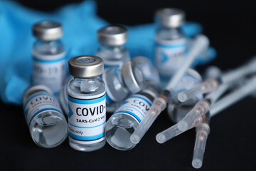 COVID 19 vaccine bottles, sealed injections and blue medical glove on black background