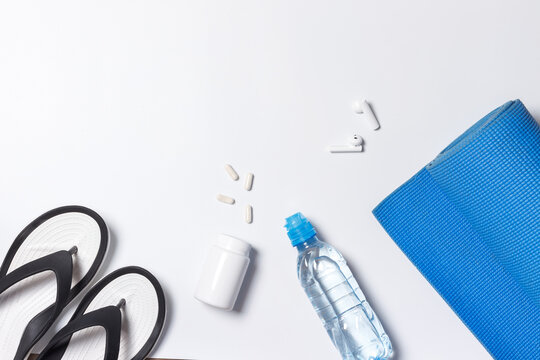 Sports accessories, sports nutrition. Exercise mat, flip-flops, bottled water and capsules with sports supplements