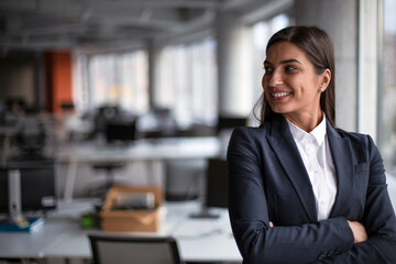 Portrait of a smiling businesswoman standing arm crossed in open space office. 