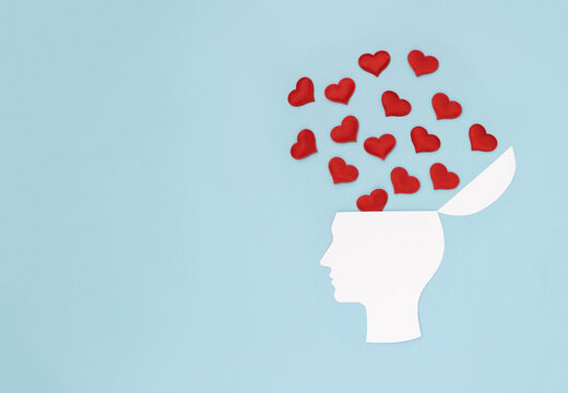 Silhouette of human's head made of white cardboard on blue background decorated with red hearts. Crazy with love. Copy space.