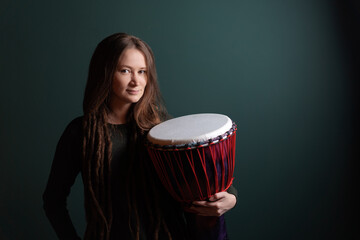 Percussion musician. Pretty young woman holding djembe. Green background.