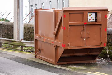 Advanced electrical powered rubbish trash skip bin in a street. Brown color. Control panel in the back. Construction and renovation business. Lock on the handeles