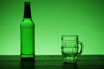 Green bottle of lager and beer glass on a wooden bar surface. Green colored. Saint Patrick background