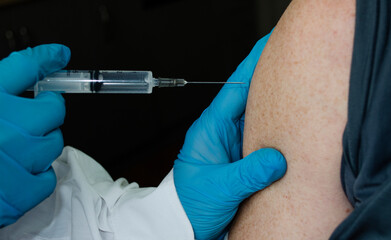 Blurred hands with a syringe injecting the vaccine into the shoulder.Vaccination procedure. Human vaccination process against coronavirus. A selective focus shot of a vaccine injection. 