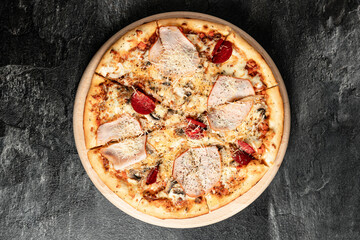 Hot tasty traditional italian pizza with salami, meat, cheese, tomatoes greens on a dark background