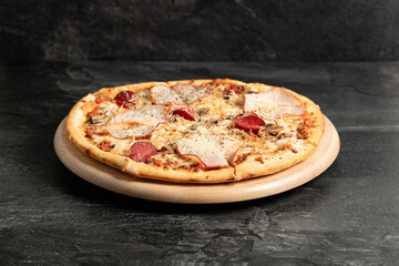 Hot tasty traditional italian pizza with salami, meat, cheese, tomatoes greens on a dark background