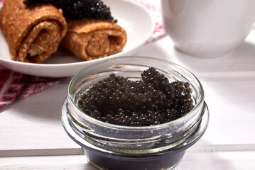 Fototapeta na wymiar A glass jar of black caviar on a white wooden background. Traditional food for Maslenitsa