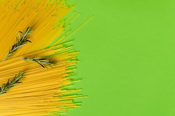 Yellow long spaghetti, rosemary sprigs on a light green background. Yellow Italian pasta. Long spaghetti. Raw spaghetti bolognese. Food concept background. Italian food and menu concept.