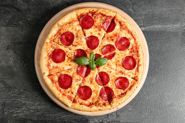 Hot tasty traditional italian pizza with salami, meat, cheese, tomatoes greens on a dark background