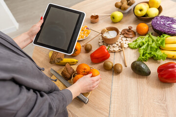Young beautiful woman using a tablet computer to cook in her kitchen, healthy food.