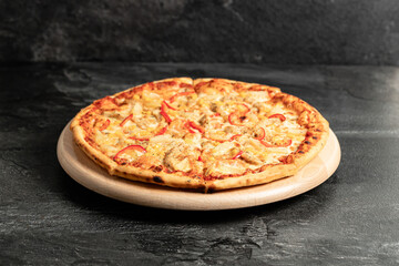 Hot tasty traditional italian pizza with salami, meat, cheese, tomatoes greens on a dark background