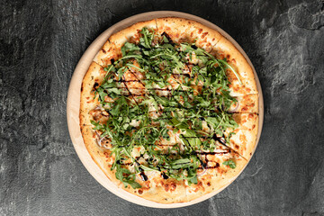 Hot tasty traditional italian pizza with salami, meat, cheese, tomatoes greens on a dark background