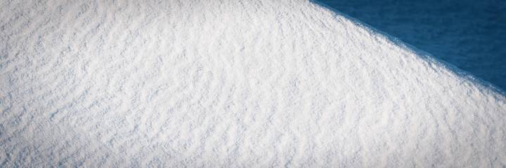 Beautiful winter background with snowy ground. Natural snow texture. Wind sculpted patterns on snow surface. Wide panoramic texture for background and design. Closeup top view with copy space.
