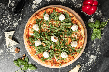 Hot tasty traditional italian pizza with salami, meat, cheese, tomatoes greens on a dark background