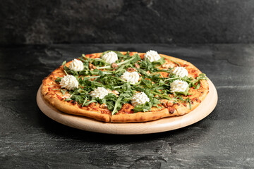 Hot tasty traditional italian pizza with salami, meat, cheese, tomatoes greens on a dark background