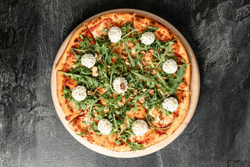 Hot tasty traditional italian pizza with salami, meat, cheese, tomatoes greens on a dark background