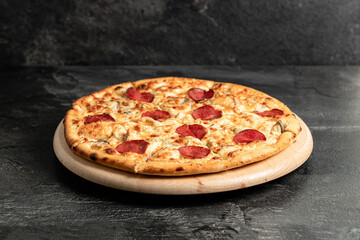 Hot tasty traditional italian pizza with salami, meat, cheese, tomatoes greens on a dark background