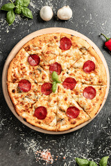 Hot tasty traditional italian pizza with salami, meat, cheese, tomatoes greens on a dark background