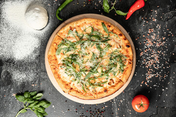 Hot tasty traditional italian pizza with salami, meat, cheese, tomatoes greens on a dark background