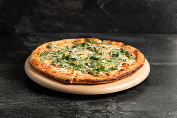 Hot tasty traditional italian pizza with salami, meat, cheese, tomatoes greens on a dark background
