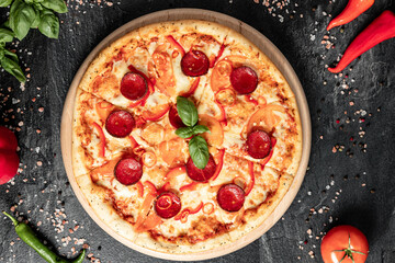 Hot tasty traditional italian pizza with salami, meat, cheese, tomatoes greens on a dark background