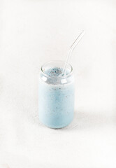Blue milk drink with the addition of moth peas and flax seeds in a glass jar with a straw on a white background