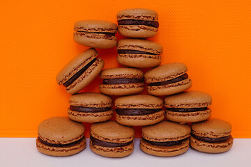 Homemade Chocolate cocoa macaron cookies filled with chocolate hazelnut ganache on an orange background