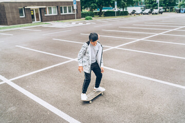 Fototapeta premium Teenager skateboarder boy riding a skateboard on asphalt playground with white lines doing tricks. Youth generation Freetime spending concept image.