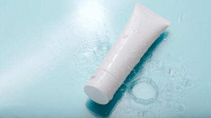 White cosmetic product in tube on color blue background with water drops. Mock up skincare cosmetic...