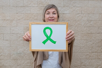Woman holds a sign with a green ribbon for awareness and support of people living with disease....