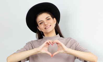 Pretty romantic young woman making a heart gesture with her fingers in front of her chest showing her love and affection with a happy tender smile