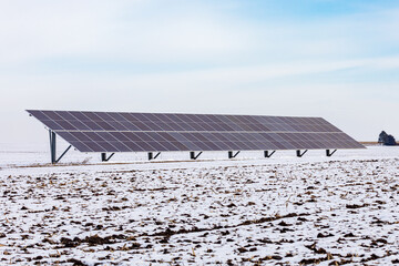 Ground mounted solar panels in snow covered farm field on cloudy day. Concept of renewable energy,...