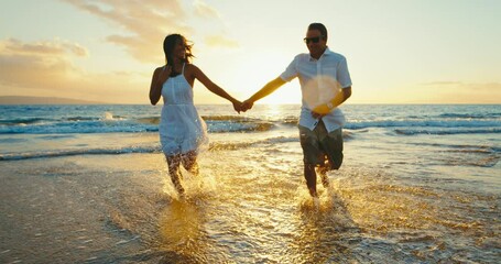 Happy couple in love, playing on the beach at sunset, running and splashing in the waves, travel vacation lifestyle.
